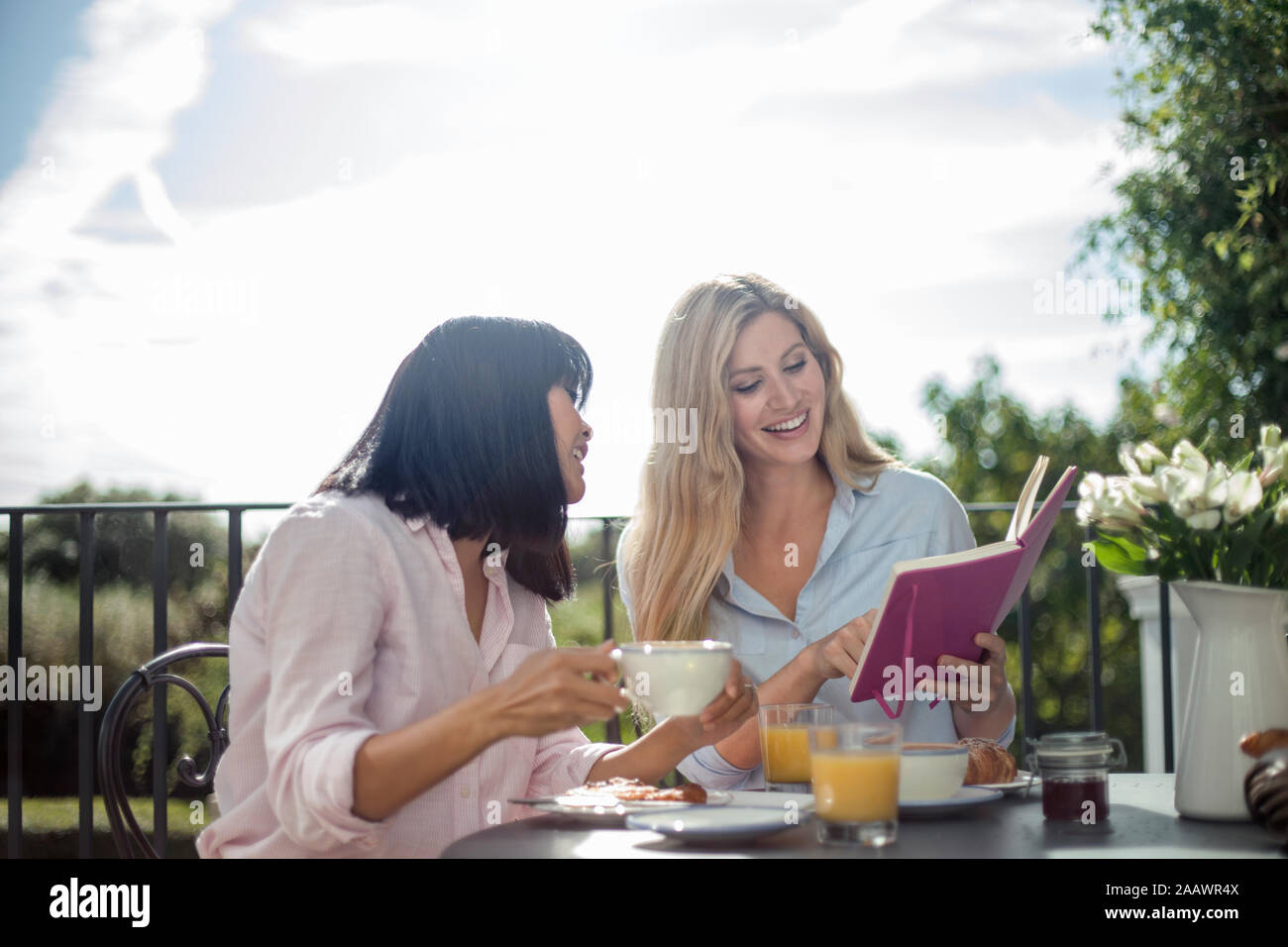 Due donne di fare colazione in outdoor cafe tabella libro di lettura Foto Stock