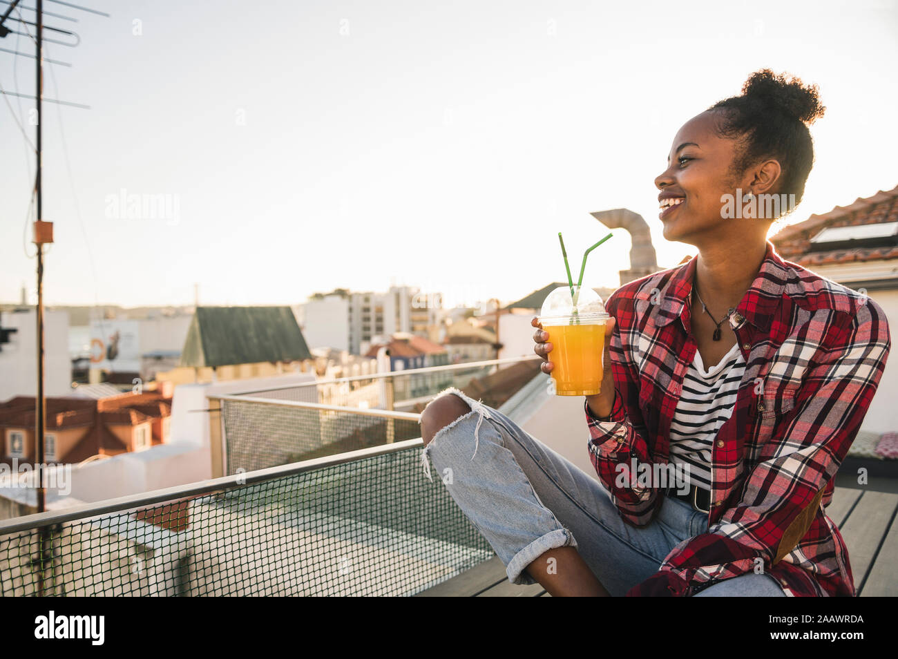 Felice giovane donna con un drink sulla terrazza sul tetto al tramonto Foto Stock