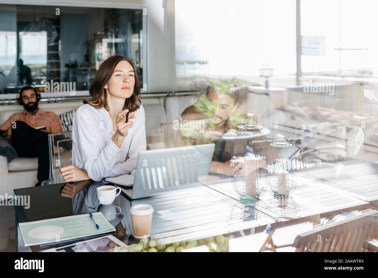 I suoi collaboratori utilizzando computer portatile sul tavolo dietro il vetro di finestra Foto Stock