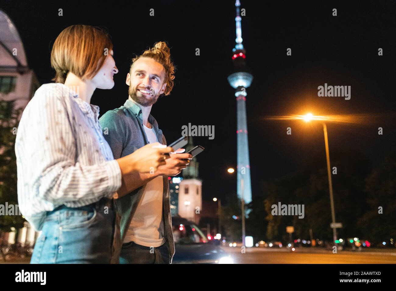 Felice coppia utilizzando gli smartphone della città di notte, Fernsehturm in background, Berlino, Germania Foto Stock