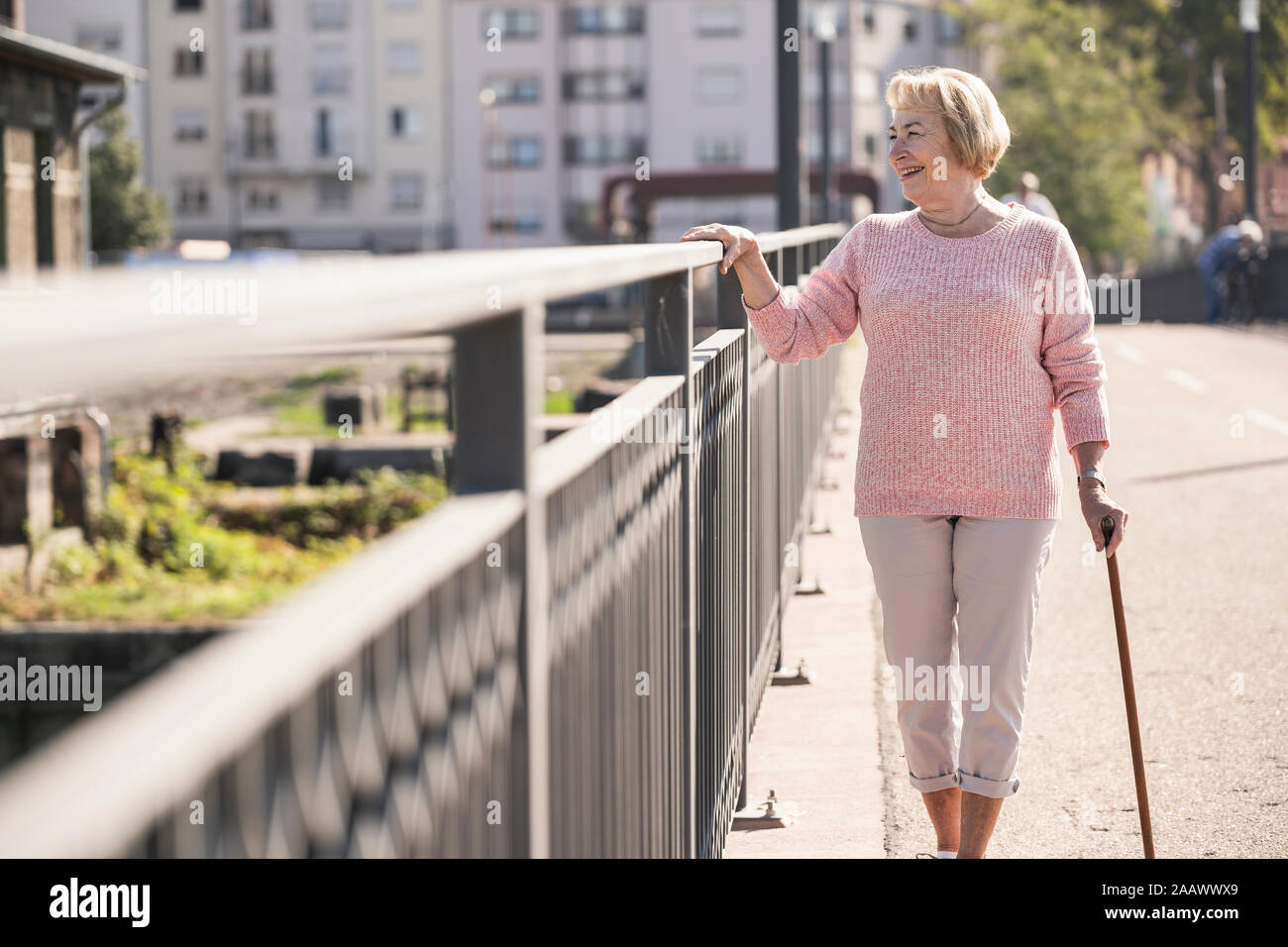 Senior Donna che cammina sulla passerella, usando un bastone, guardando lontano Foto Stock