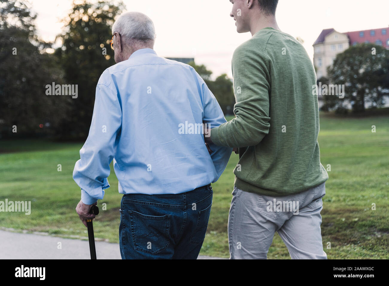 Vista posteriore del giovane uomo che assiste il suo nonno a camminare in un parco Foto Stock