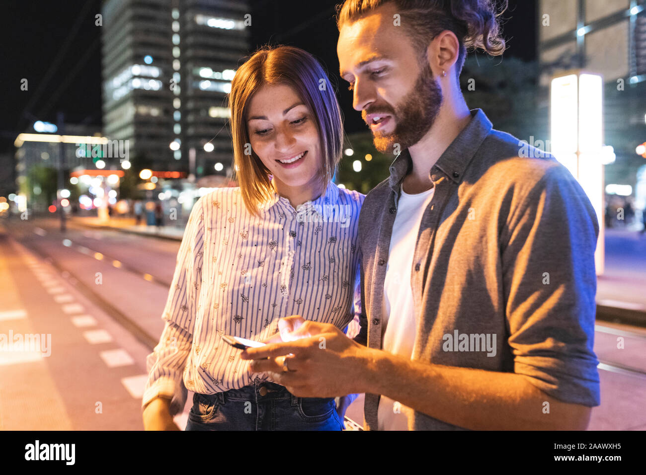 Coppia felice nella città di notte di controllo sui loro telefoni, Berlino, Germania Foto Stock