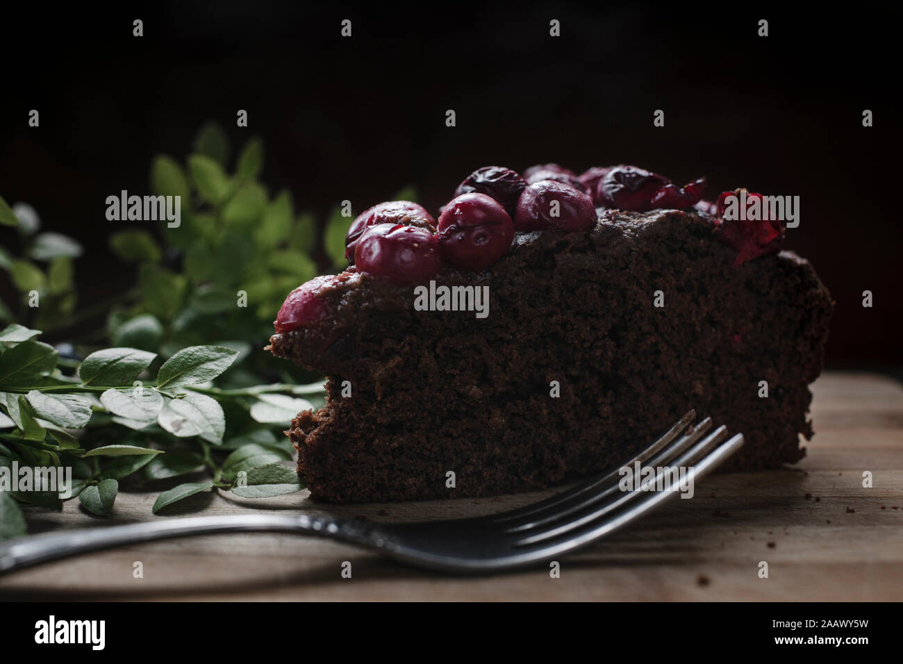 Close-up di ciliegia brownie fetta di torta con le erbe sul tavolo su sfondo nero Foto Stock