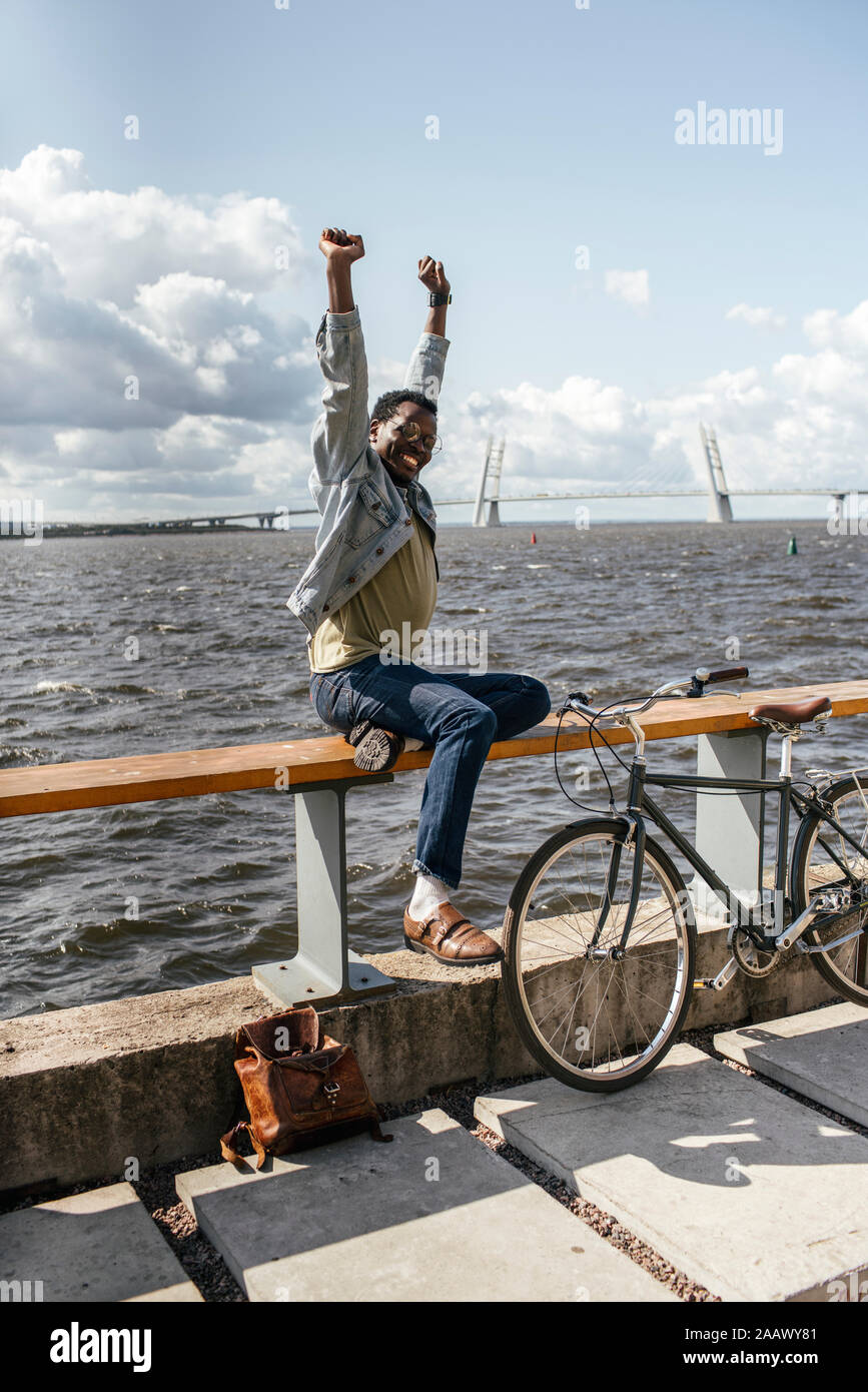 Giovane uomo con la bicicletta, seduti su railng dal mare, stretching Foto Stock