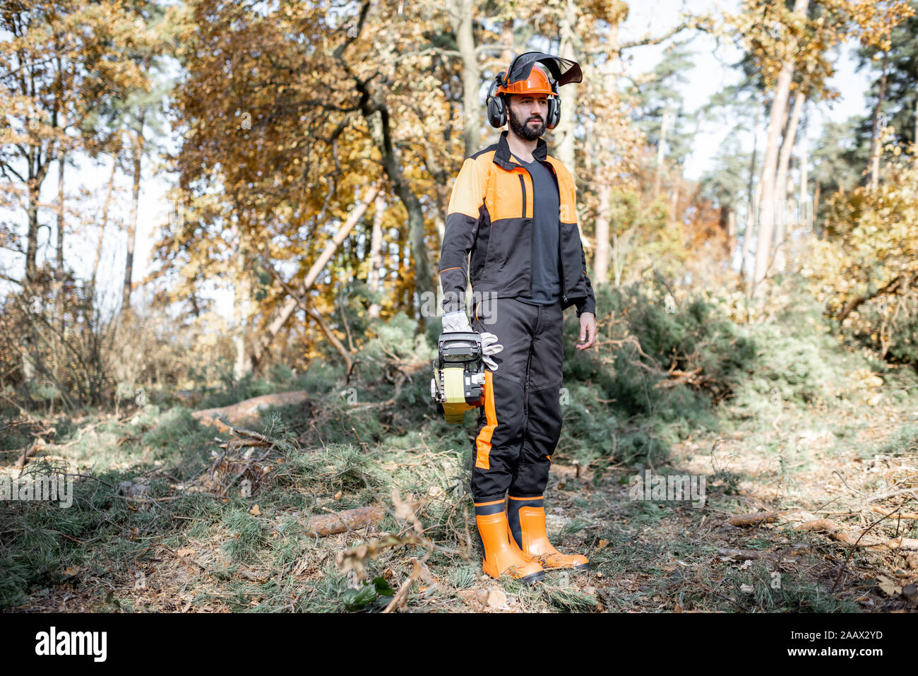A piena lunghezza Ritratto di un professionista lumberjack in indumenti da lavoro protettiva in piedi con una motosega nel bosco Foto Stock