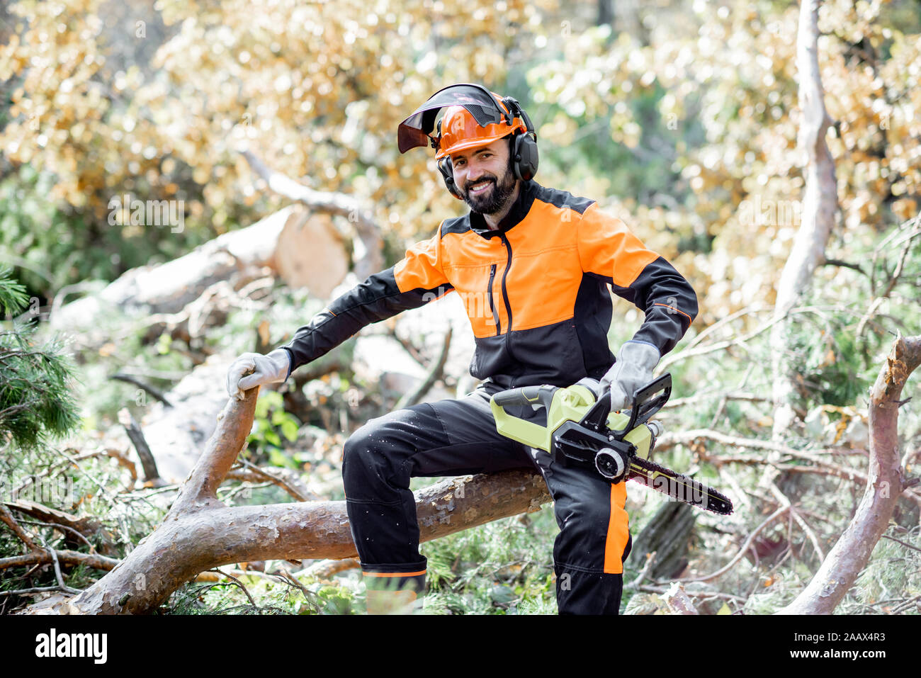 Ritratto di un professionista lumberman in indumenti da lavoro protettiva seduto con un chainsaw sull'albero abbattuto, riposo dopo il duro lavoro della foresta Foto Stock
