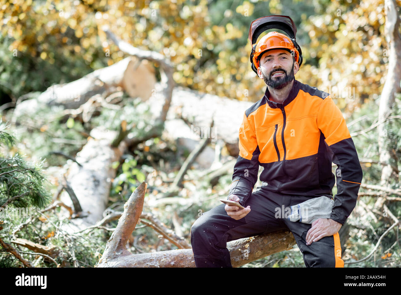 Ritratto di un professionista lumberman in indumenti da lavoro protettiva seduto sull'albero abbattuto durante il riposo dopo il duro lavoro della foresta Foto Stock