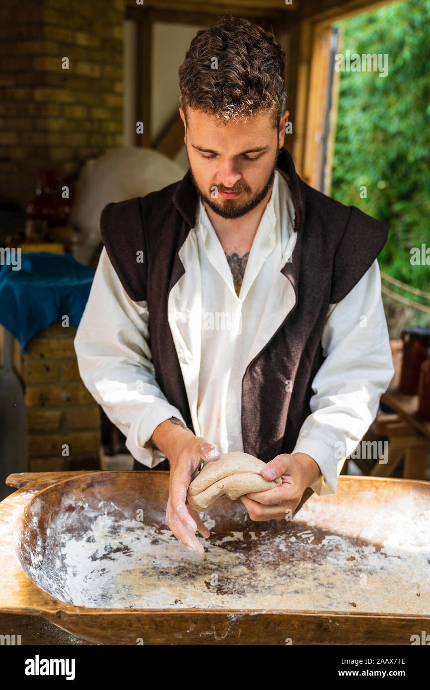 Medievale storia vivente evento a sandwich, Inghilterra. Giovane uomo rivolta verso il visualizzatore, in piedi di fronte a contrastare gli impasti più oblunga trogolo di legno. Foto Stock