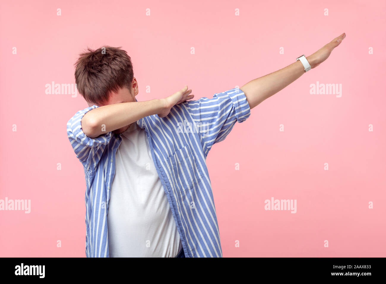 Ritratto di anonimo i capelli castani uomo nel casual camicia a righe con arrotolata permanente del manicotto in dab danza pongono, internet meme, celebrando il successo. i Foto Stock