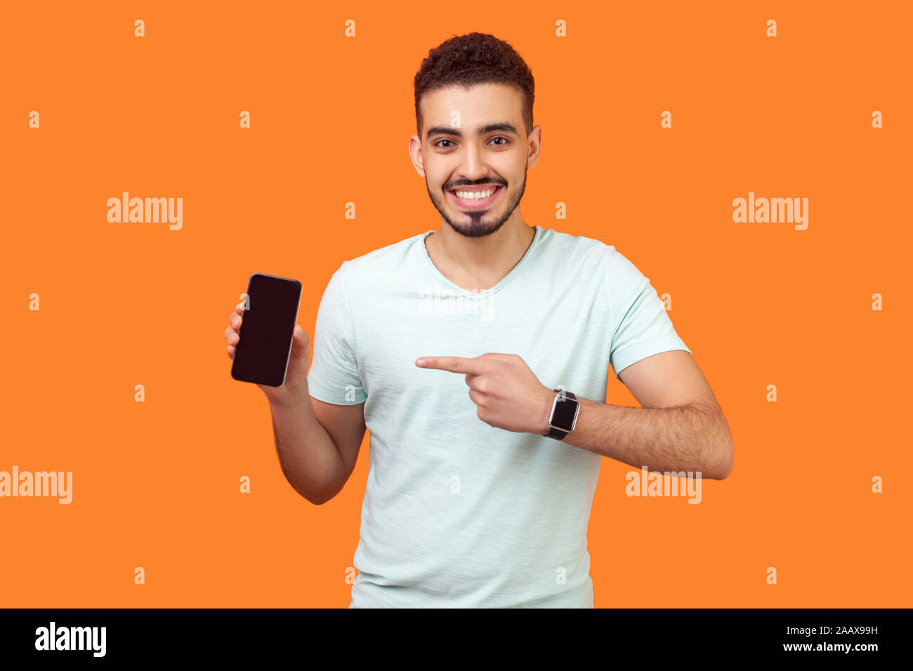 Ritratto di soddisfatto brunette uomo con la barba bianca t-shirt puntando al cellulare e sorridente alla fotocamera, raccomandare gadget o applicazione mobile. Foto Stock