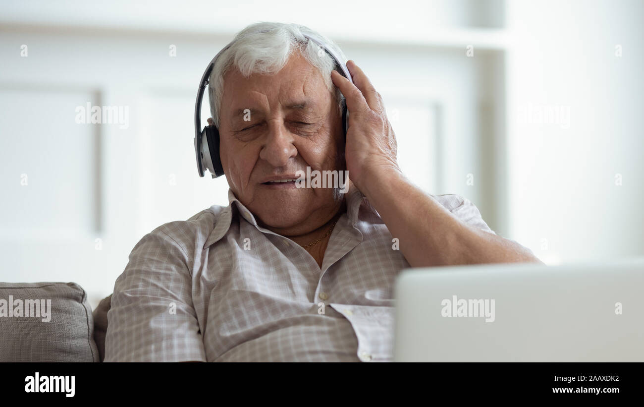 Vecchio uomo felice di indossare le cuffie wireless, godendo della musica preferita. Foto Stock