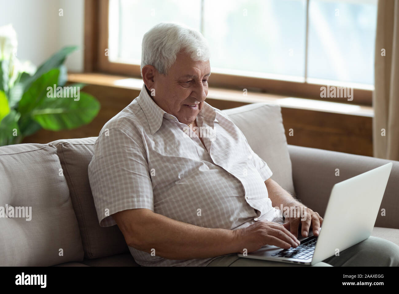 Piacevole senior 70s uomo seduto sul divano con il computer. Foto Stock