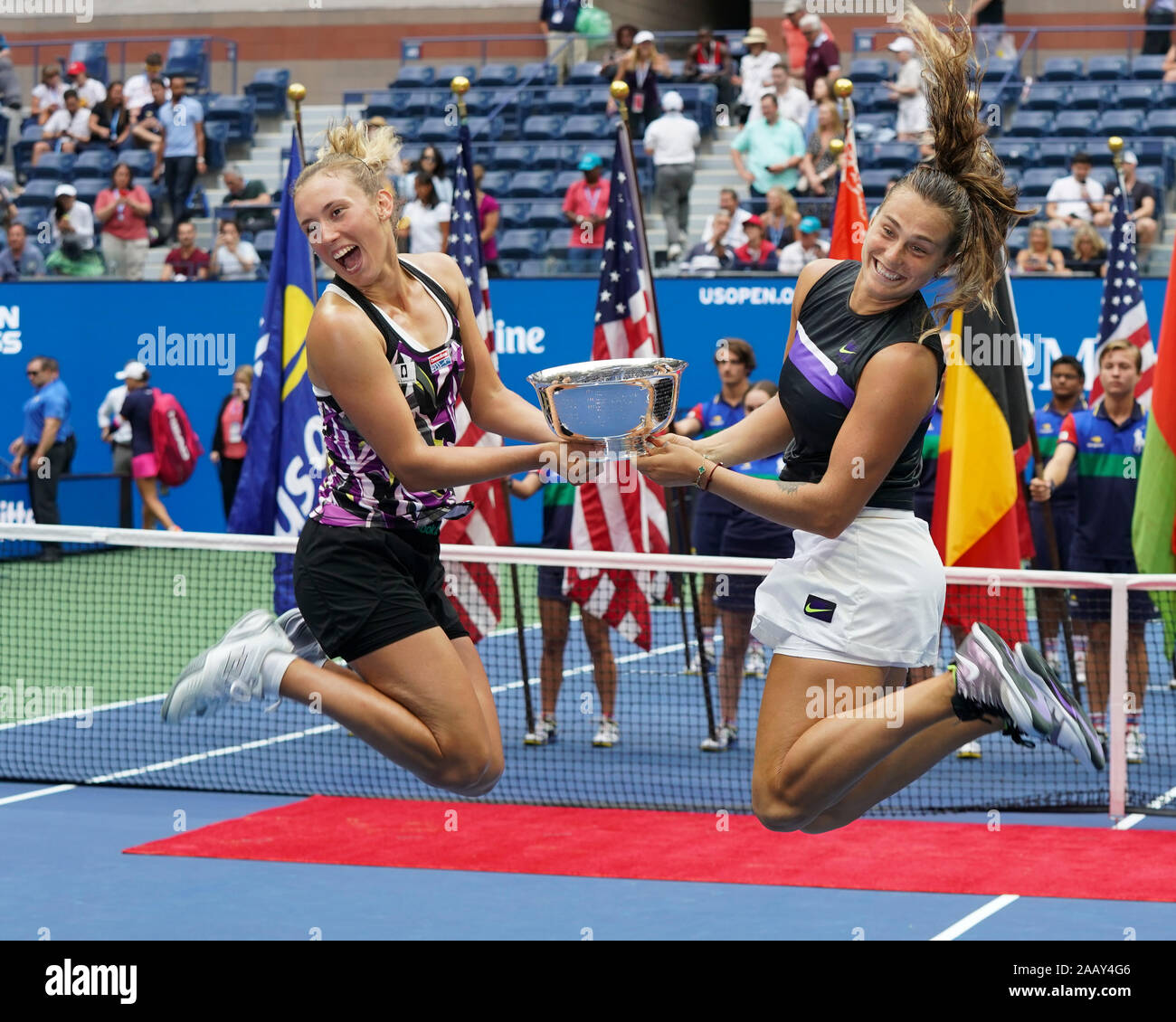 Vista laterale di Aryna Sabalenka e Elise Mertens jumping tenendo trofeo durante la presentazione del trofeo nel 2019 US Open Tennis Tournament, New York Cit Foto Stock