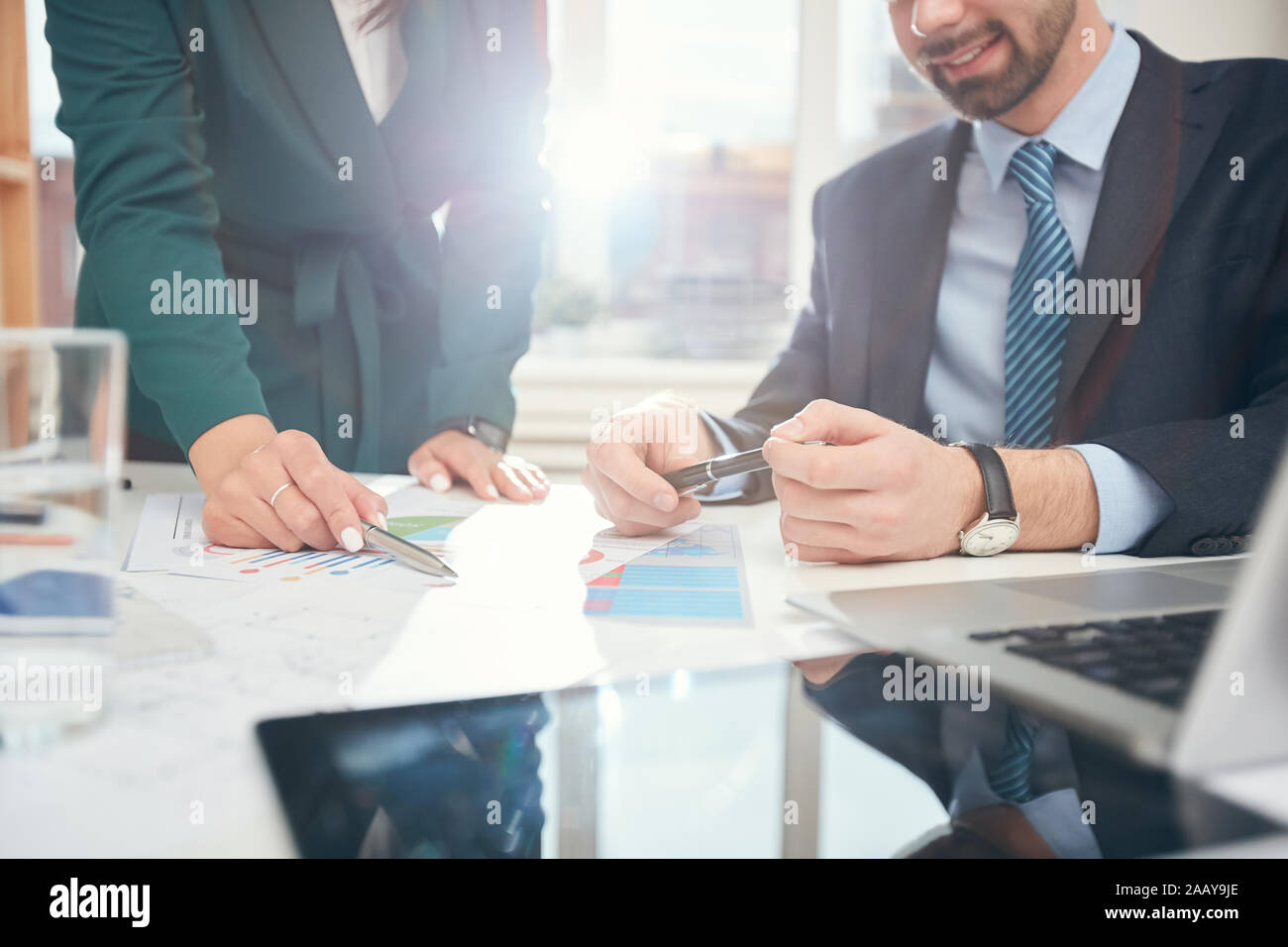 Immagine di sfondo di due business di successo di persone che puntano a dati grafici e tabelle durante la riunione in ufficio, scena illuminata dalla luce del sole, spazio di copia Foto Stock