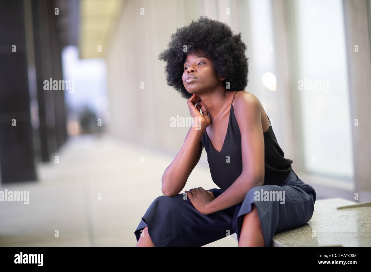 Piuttosto giovane americano africano donna su strade cittadine, seduta sul banco di lavoro Foto Stock