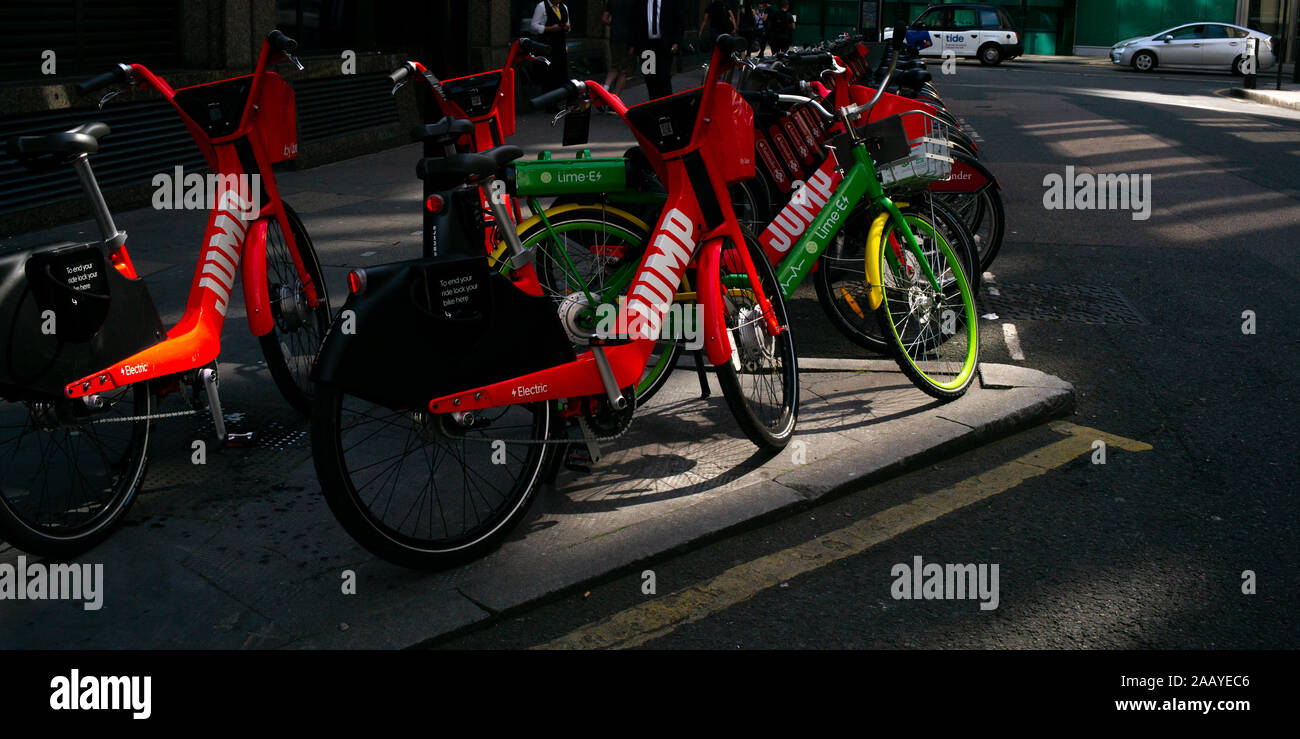 Un calce-E e salto di assistenza elettrica ciclo stazione di condivisione con le biciclette parcheggiate fino in con i colori vivaci in piedi fuori al mattino presto sun Foto Stock