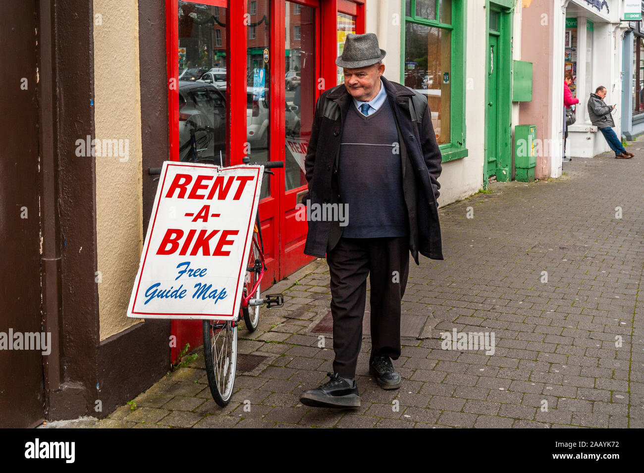 Uomo anziano passeggiate passato un noleggio bici segno su un push bike al di fuori di un negozio a Killarney, Co. Kerry, Irlanda, Foto Stock