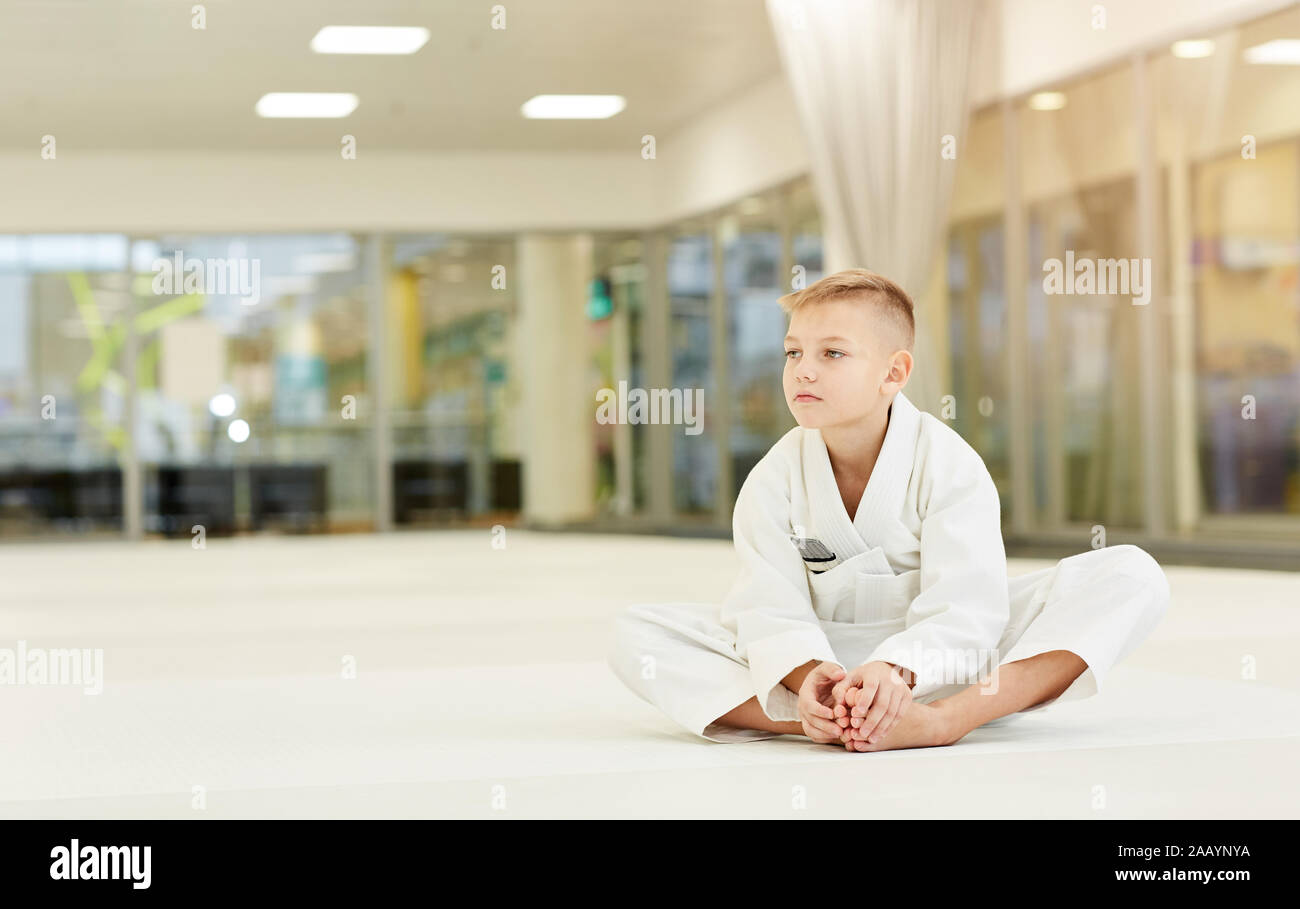 Little Boy in kimono bianco seduto sul pavimento e riposo dopo la formazione sportiva nel karate in palestra Foto Stock