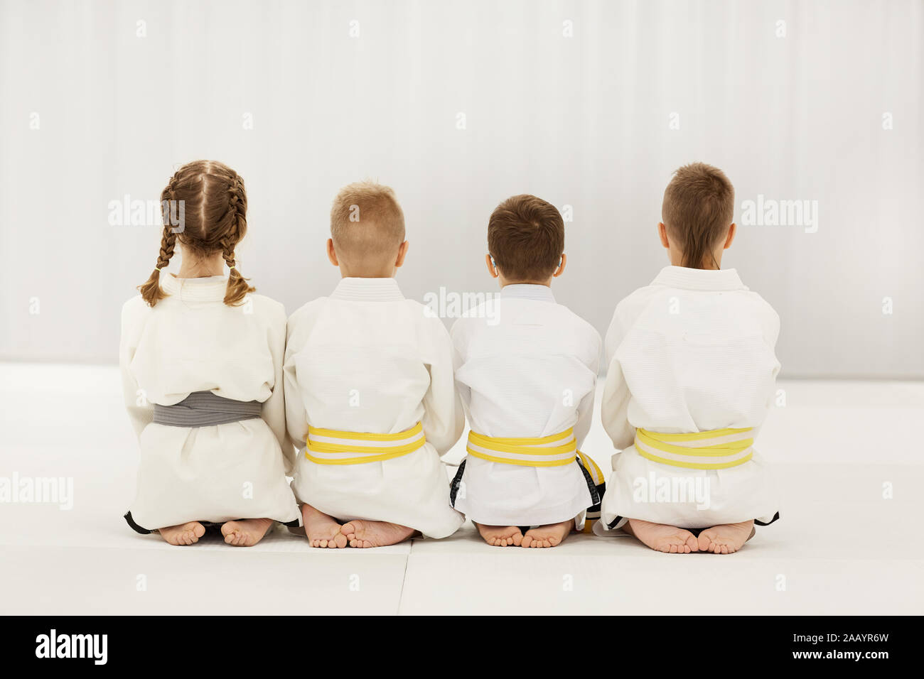 Vista posteriore dei bambini scalzi in kimono bianco seduto sul pavimento insieme in una riga Foto Stock