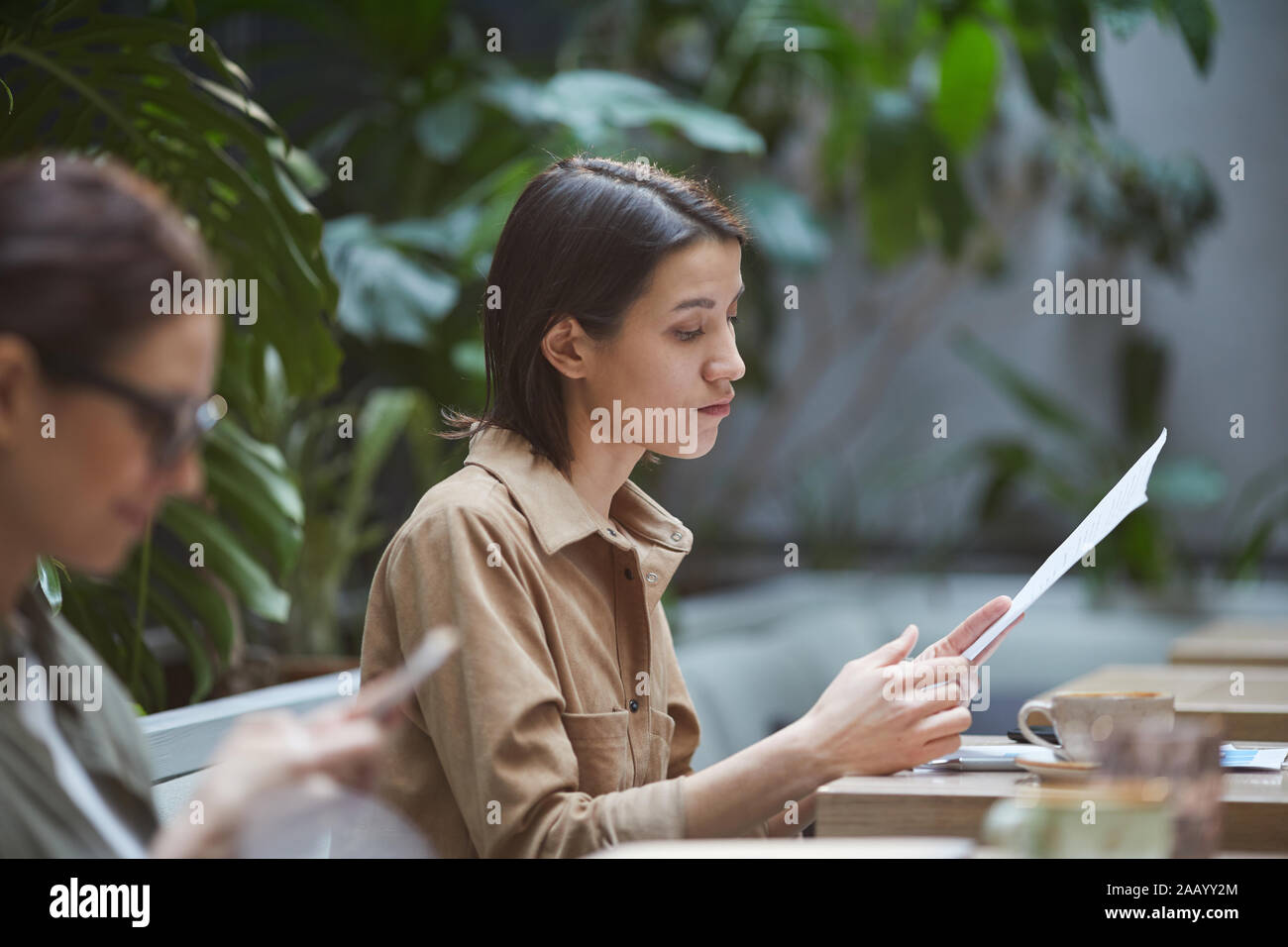 Vista laterale Ritratto di giovane imprenditrice la lettura dei documenti mentre si lavora in outdoor cafe, spazio di copia Foto Stock