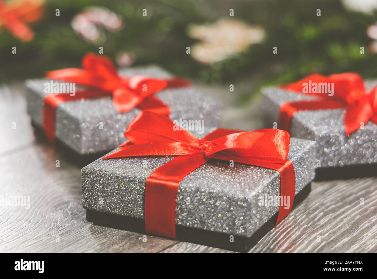 Tre d'argento regalo di Natale di scatole con nastro rosso legato in un arco intorno alla seduta in background sono i rami di un albero di Natale e decorazioni Foto Stock