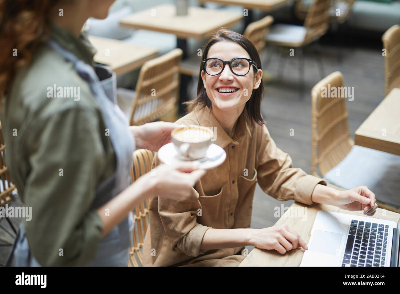 Angolo alto Ritratto di giovane donna sorridente cameriera a portare tazza di caffè mentre si lavora in cafe, spazio di copia Foto Stock