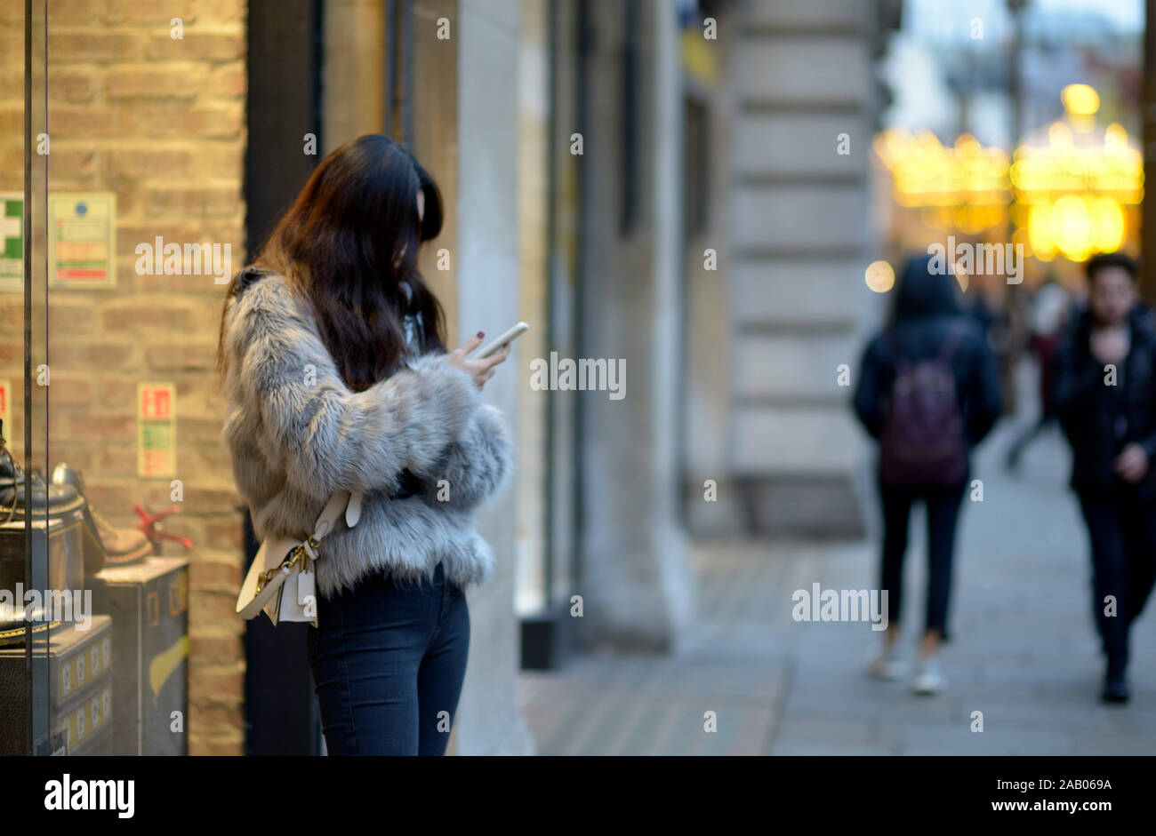 Signora giovane, nella camicia di pelliccia, controllando il suo telefono cellulare. Foto Stock