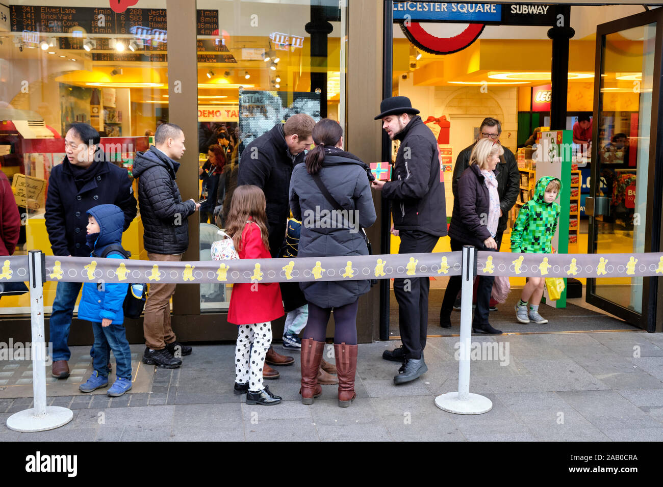 Persone in attesa in linea al di fuori della Lego, Piccadilly Square store essendo intrattenuti da dipendente di sicurezza Foto Stock
