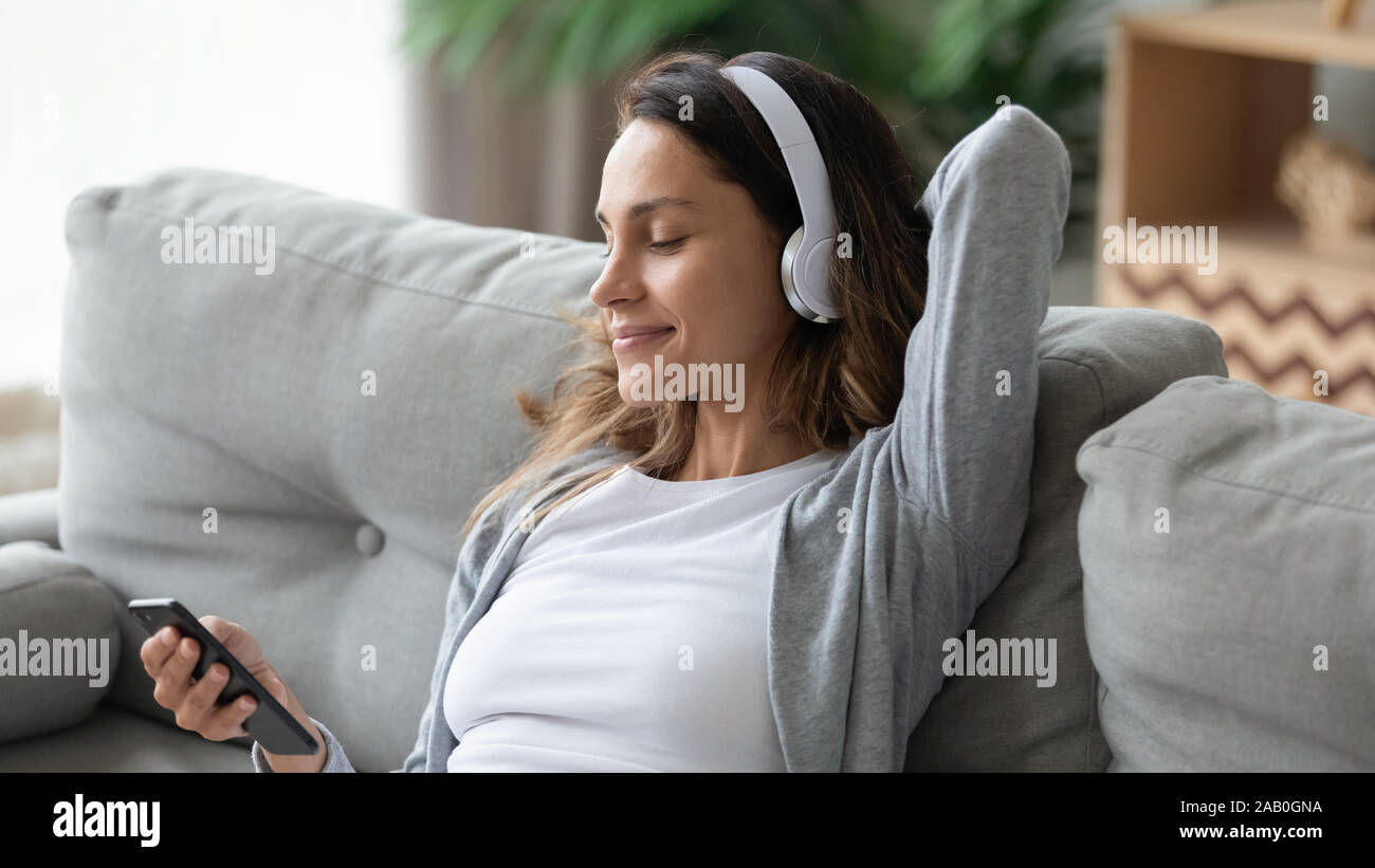 Donna che indossa le cuffie wireless ascolta musica rilassante seduto sul lettino Foto Stock