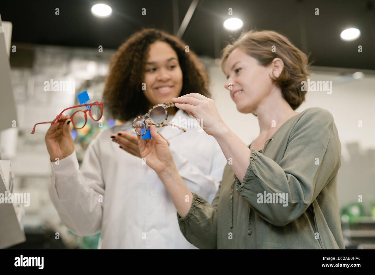 Giovani competenti mixed-consulente di gara che mostra un paio di occhiali per acquirente femmina Foto Stock