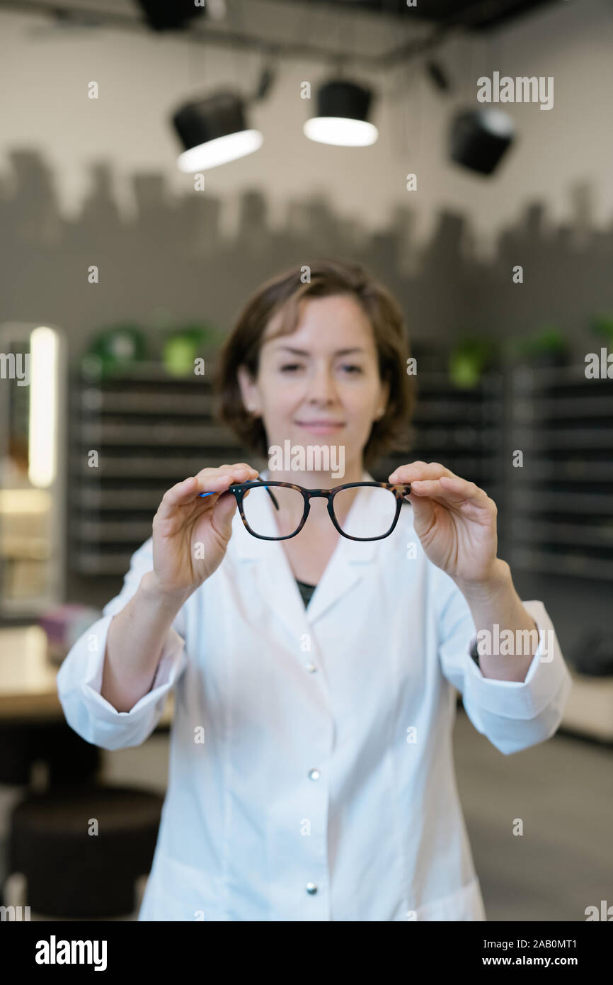 Giovane femmina professionale all'ottico optometrista in camice bianco tenendo un paio di occhiali Foto Stock