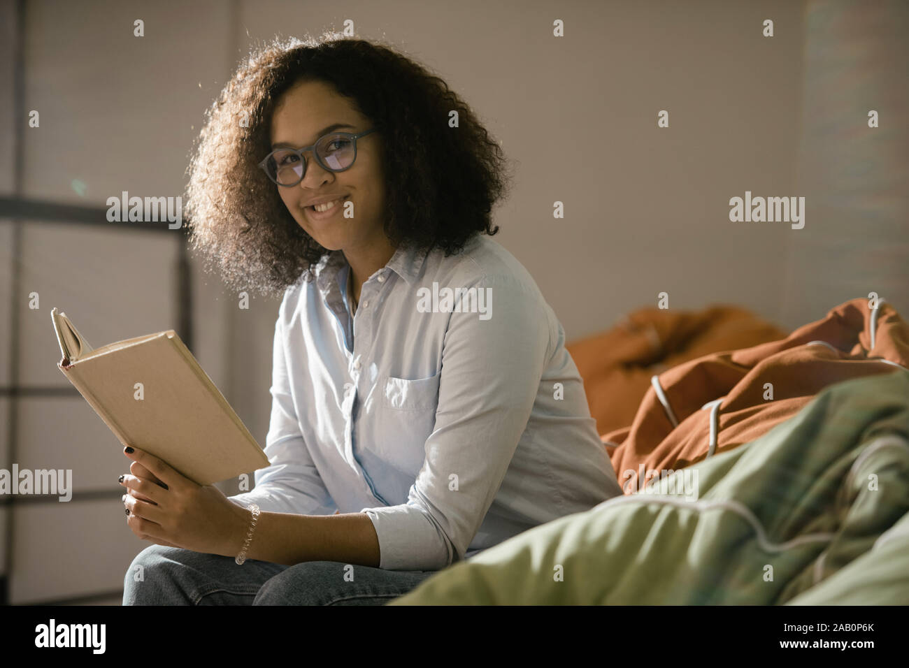 Piuttosto giovane studente sorridente con il libro aperto che vi guardano attraverso occhiali Foto Stock