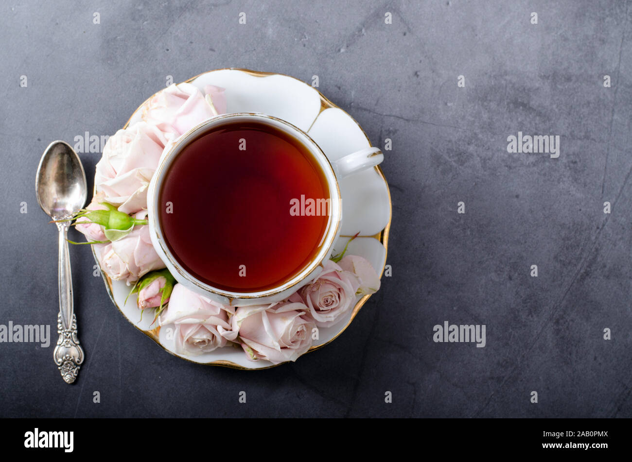 Tea time sullo sfondo. Top-down vita ancora con l'annata di colore bianco porcellana tazza da tè con delicata rosa rose e bella cucchiaino su uno sfondo grigio scuro. Roman Foto Stock