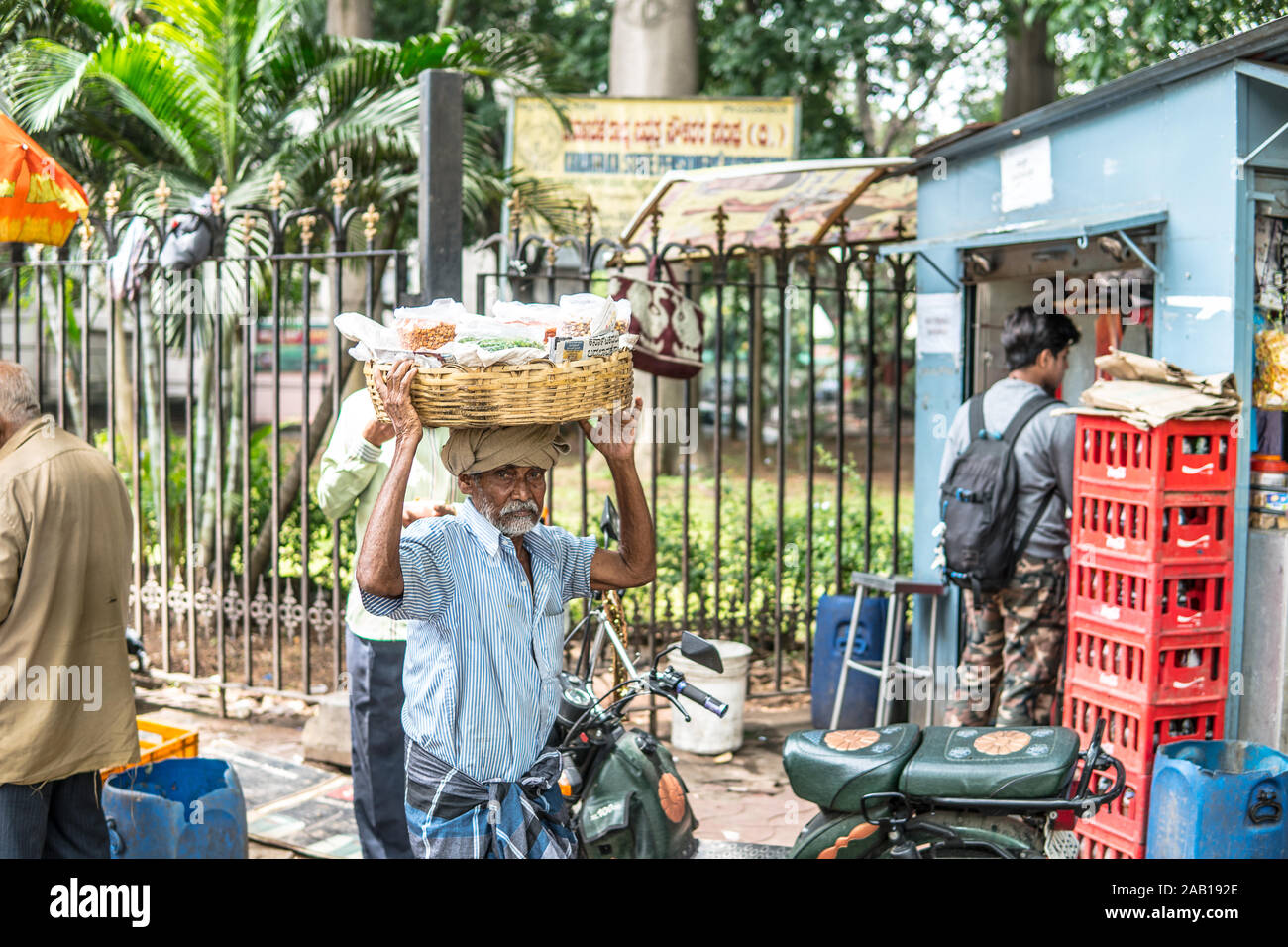 Bangalore, India, strade di Bengaluru città indiana indù vecchio uomo che porta il cestello con arachidi in vendita sulla testa, vestito di lungi Foto Stock
