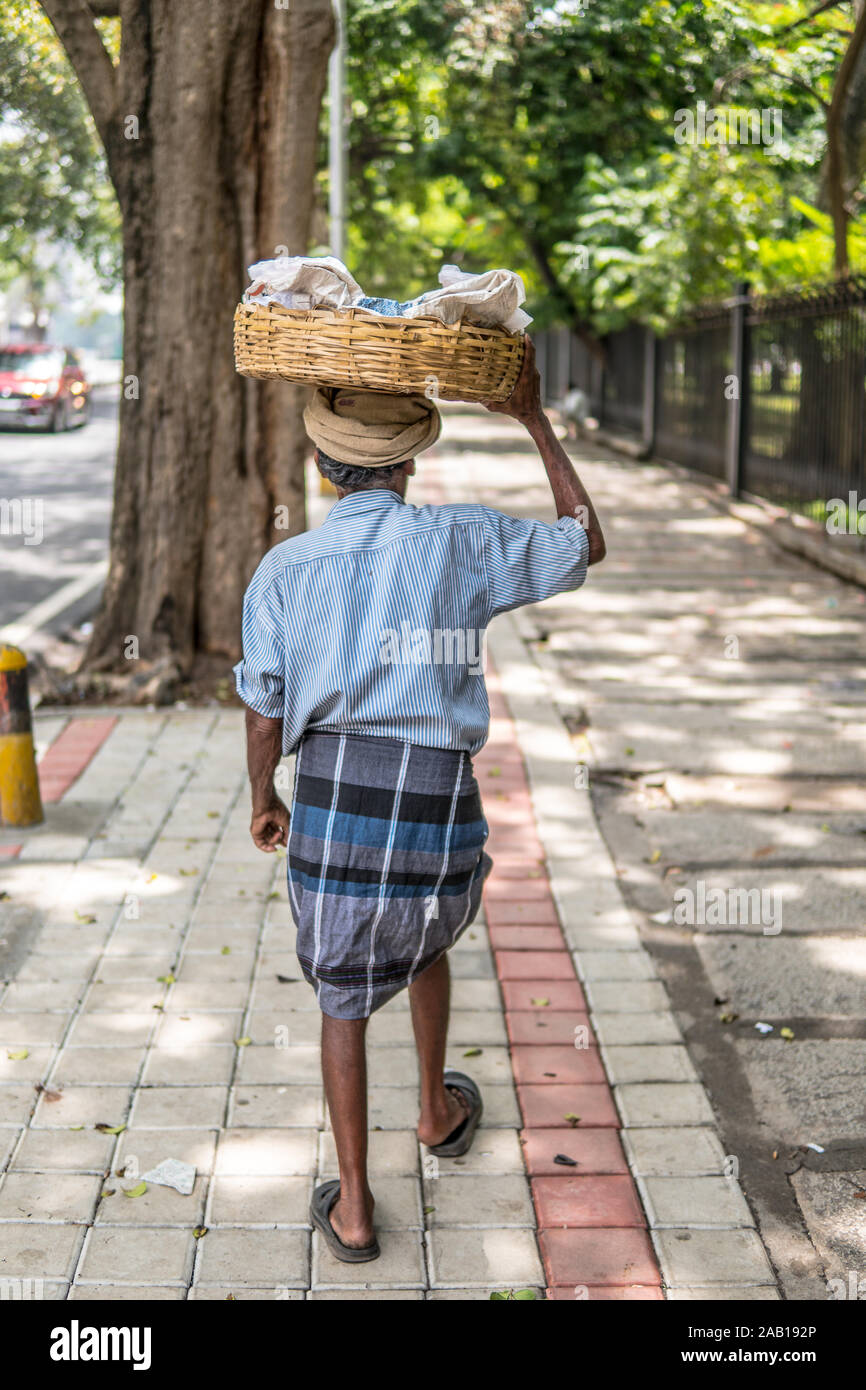 Bangalore, India, strade di Bengaluru città indiana indù vecchio uomo che porta il cestello con arachidi in vendita sulla testa, vestito di lungi Foto Stock
