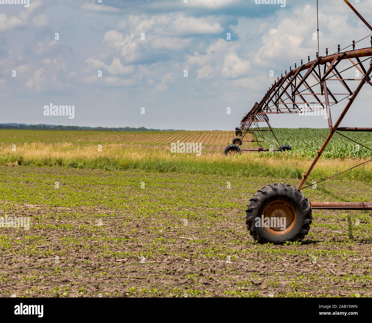 Rusty, vecchio perno centrale di un sistema di irrigazione che si estende su dolci colline tra crescente di soia e di mais di campi di fattoria. Giorno d'estate e di sole con le nuvole Foto Stock