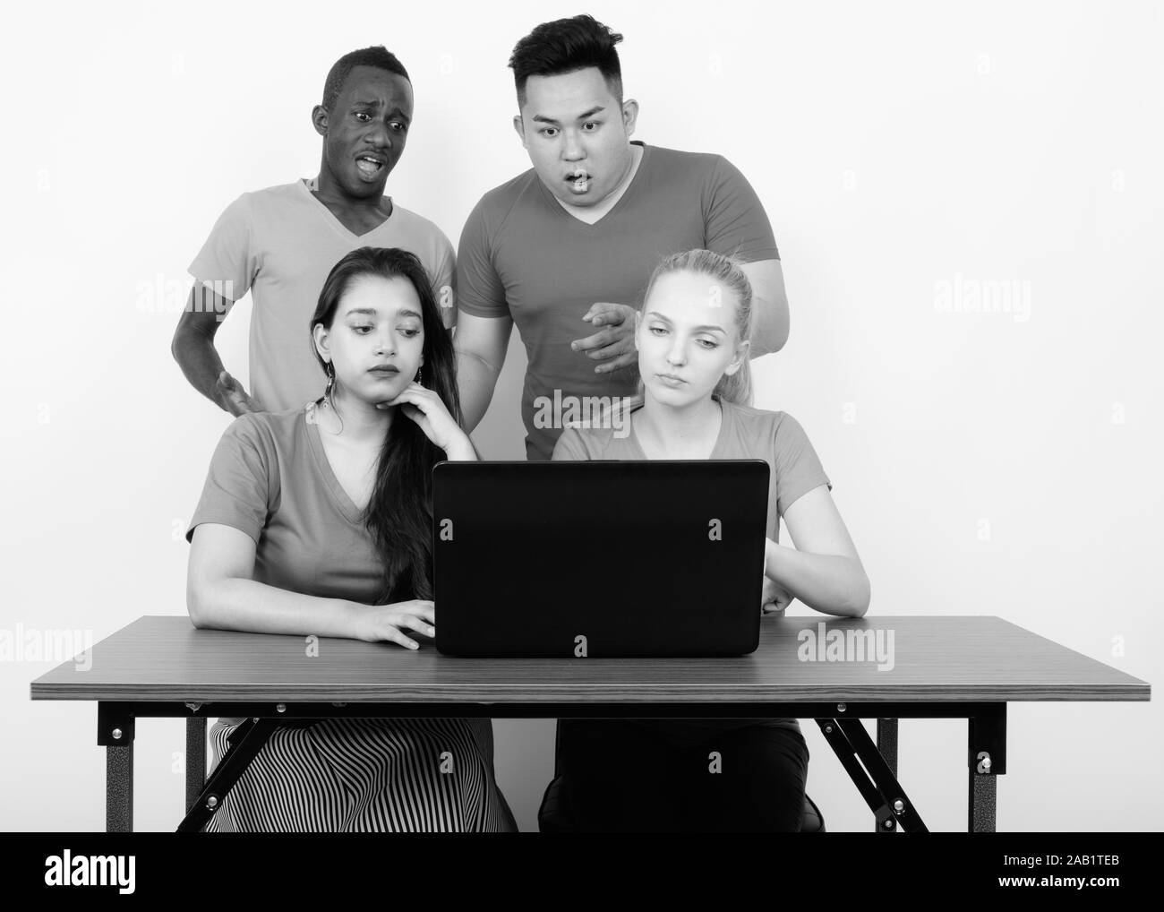 Studio shot del variegato gruppo di multi etnico amici utilizzando computer portatile sul tavolo di legno insieme con gli amici in cerca sconvolto per il retro Foto Stock