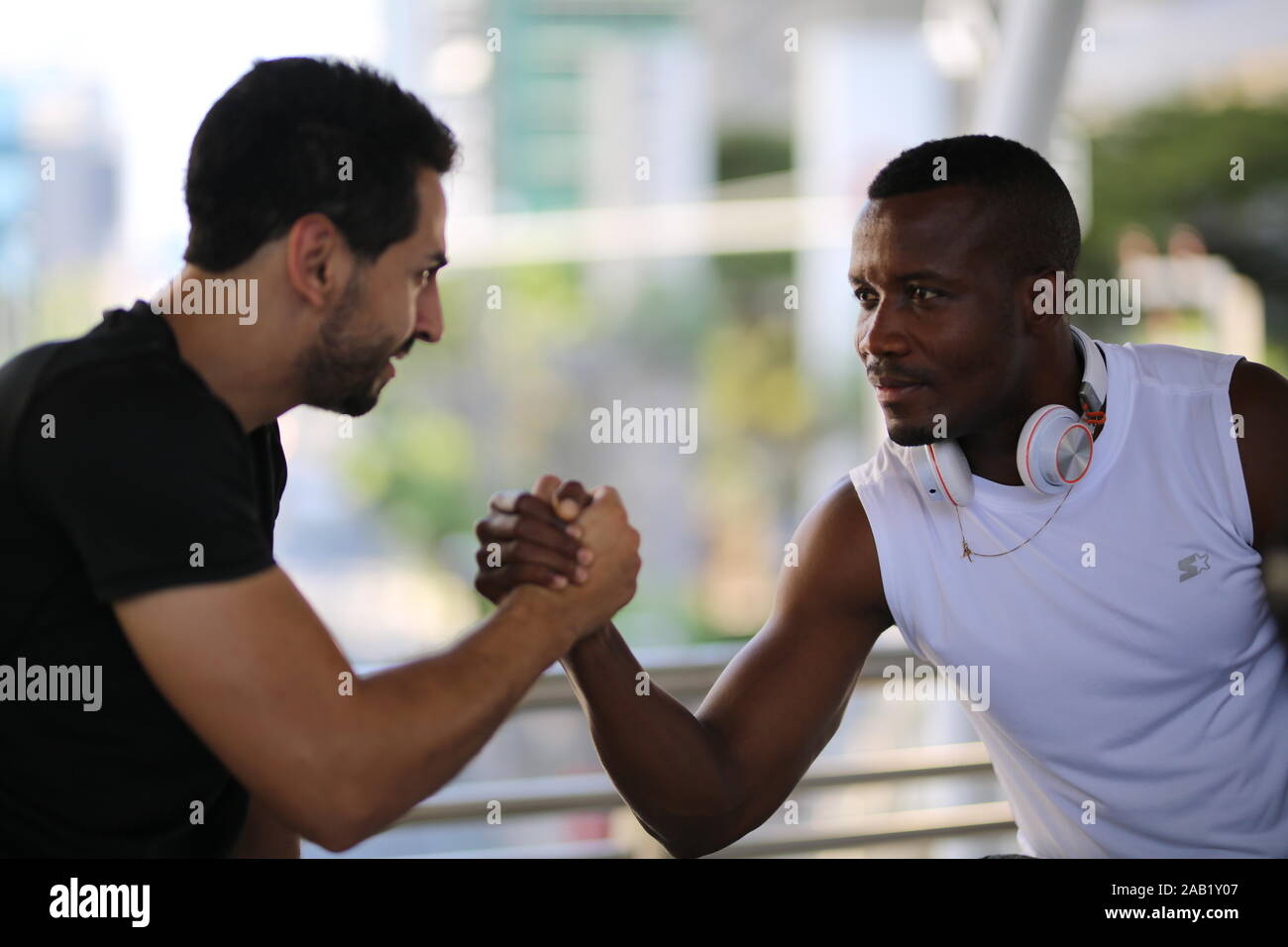 Fitness, sport, esercizio e concetto di stile di vita - due mix di uomo-gara nella seduta di abbigliamento sportivo per il relax e lo stiramento della gamba sul passo del Stadium Foto Stock