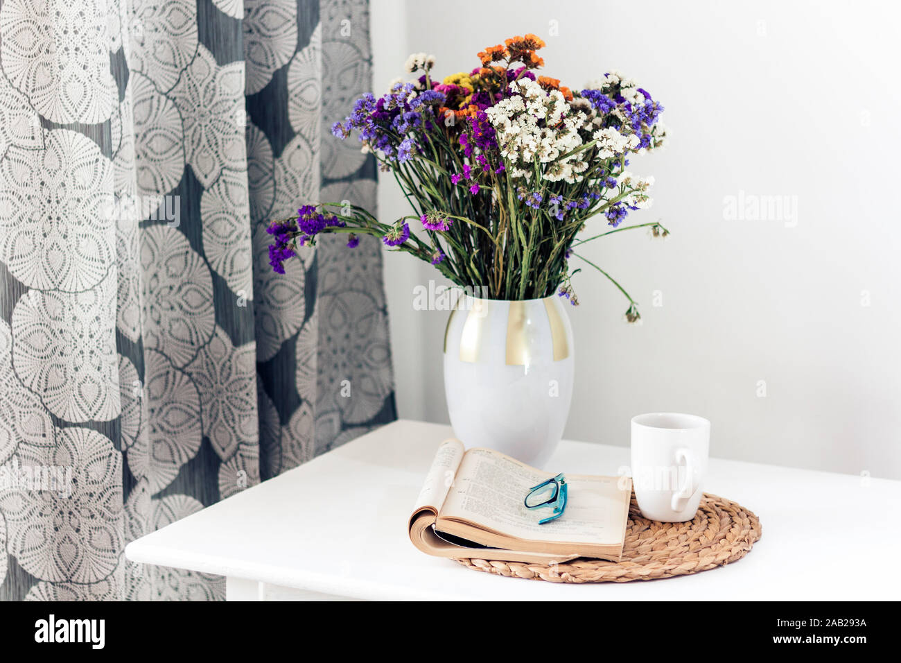 Elegante vaso in ceramica con splendidi fiori e libro aperto sul tavolo in  vimini vicino a una parete chiara Foto stock - Alamy