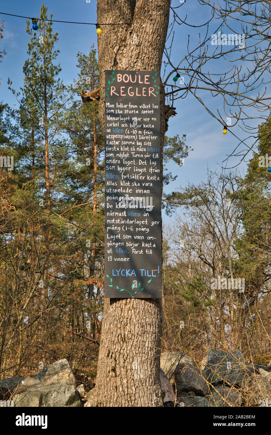 Blackboard attaccata ad un tronco di albero con regolamenti in svedese su come giocare il gioco delle bocce, Fjaderholmarna, arcipelago di Stoccolma, Svezia Foto Stock