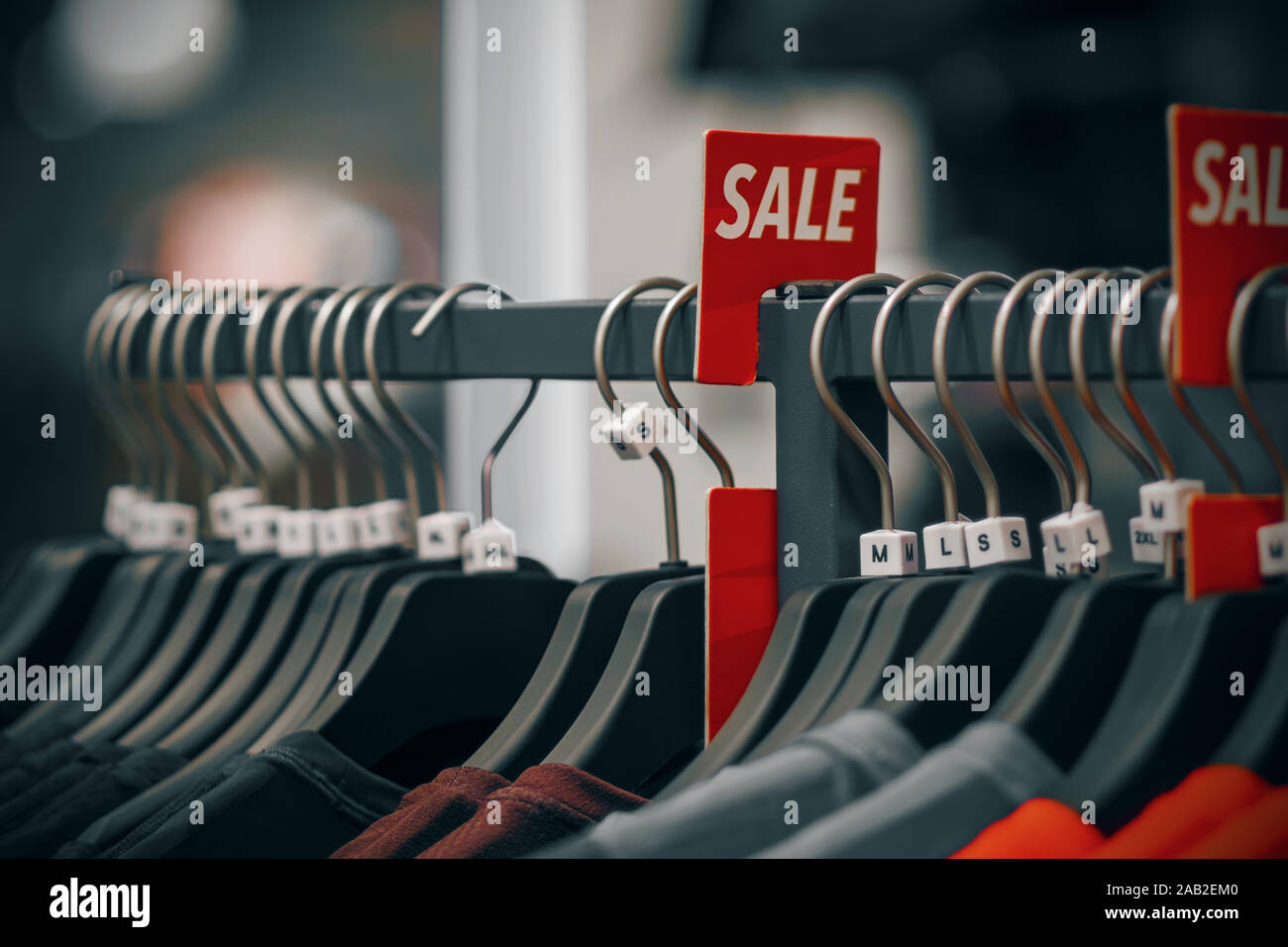 Il negozio appendere dark appendiabiti con abiti casual in diversi colori e accanto a esso pende un luminoso segno rosso-vendita. Foto Stock