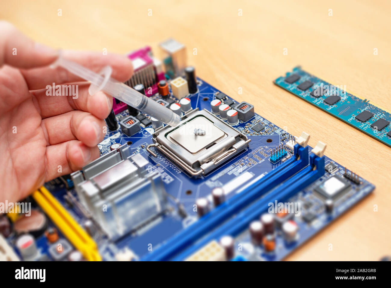Applicare la pasta termica ad un processore di un computer. Installazione del processore concetto e la soluzione di raffreddamento. Scheda madre blu e RAM memory stick accanto a. Clo Foto Stock