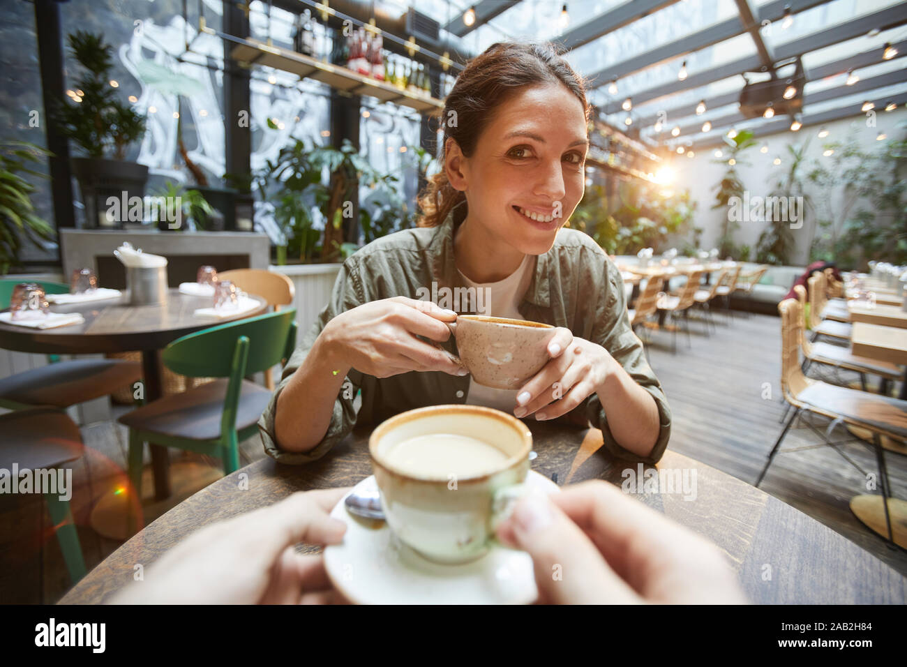 Vista fisheye del donna sorridente holding tazza da caffè a parlare con un amico in tutta la tabella in cafe, POV Foto Stock