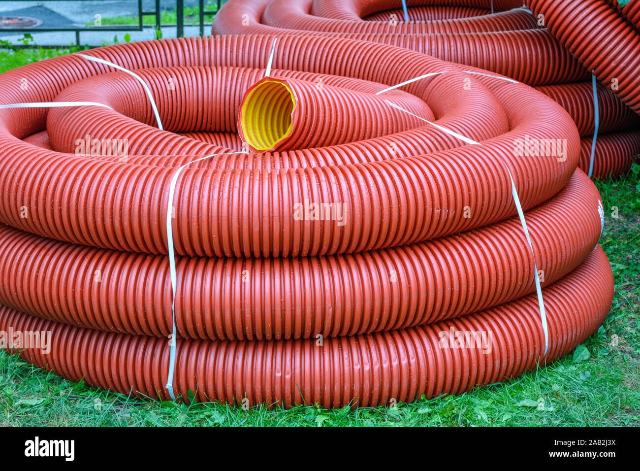 Bobine di nuova red tubo in plastica con gocce di pioggia sulla città prato  con erba verde. Rosso di tubi in plastica per cavi interrati per la  protezione. Primo piano di matassa