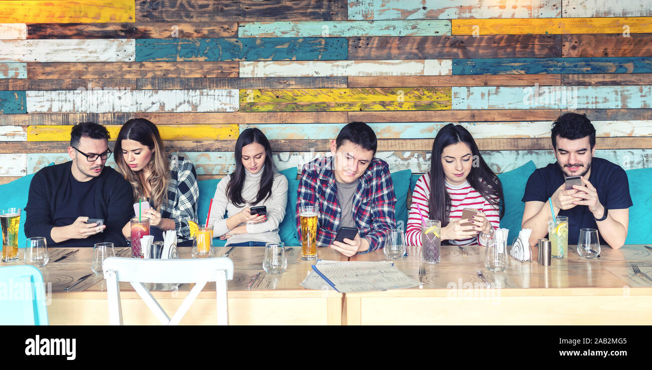 Un gruppo di giovani amici utilizzando mobile smart phone al pub ristorante tabella per i social media Foto Stock