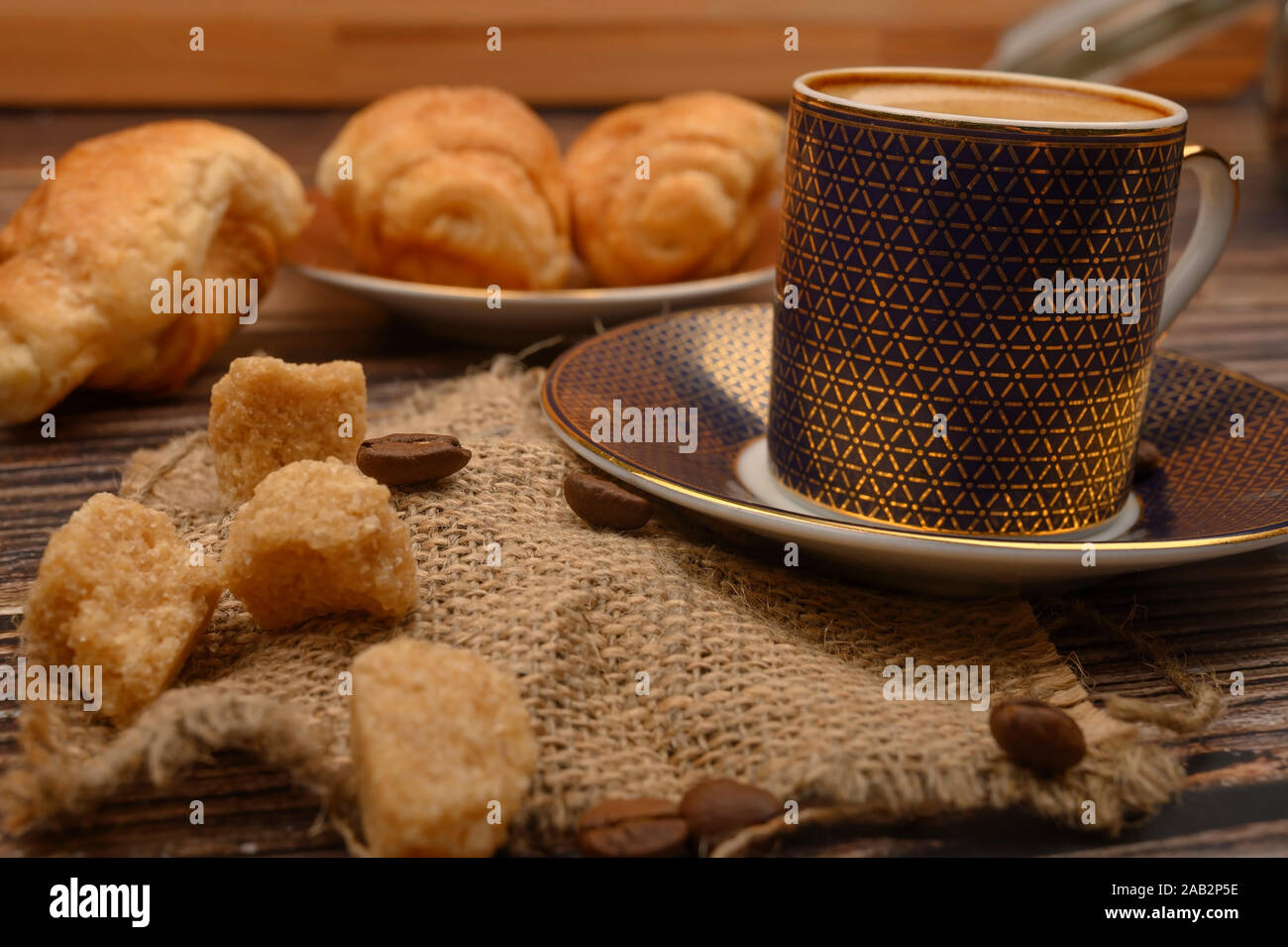 Tazza di caffè, zucchero di canna, croissant, caffè in grani su sfondo di legno. Close up Foto Stock
