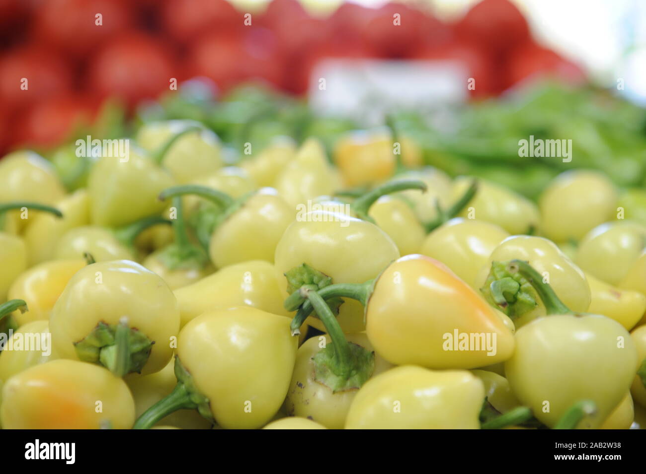 Close-up shot di baby peperoni in bianco su un mercato agricolo in stallo. Sfocato cumuli di verde e peperoni rossi sullo sfondo. Foto Stock