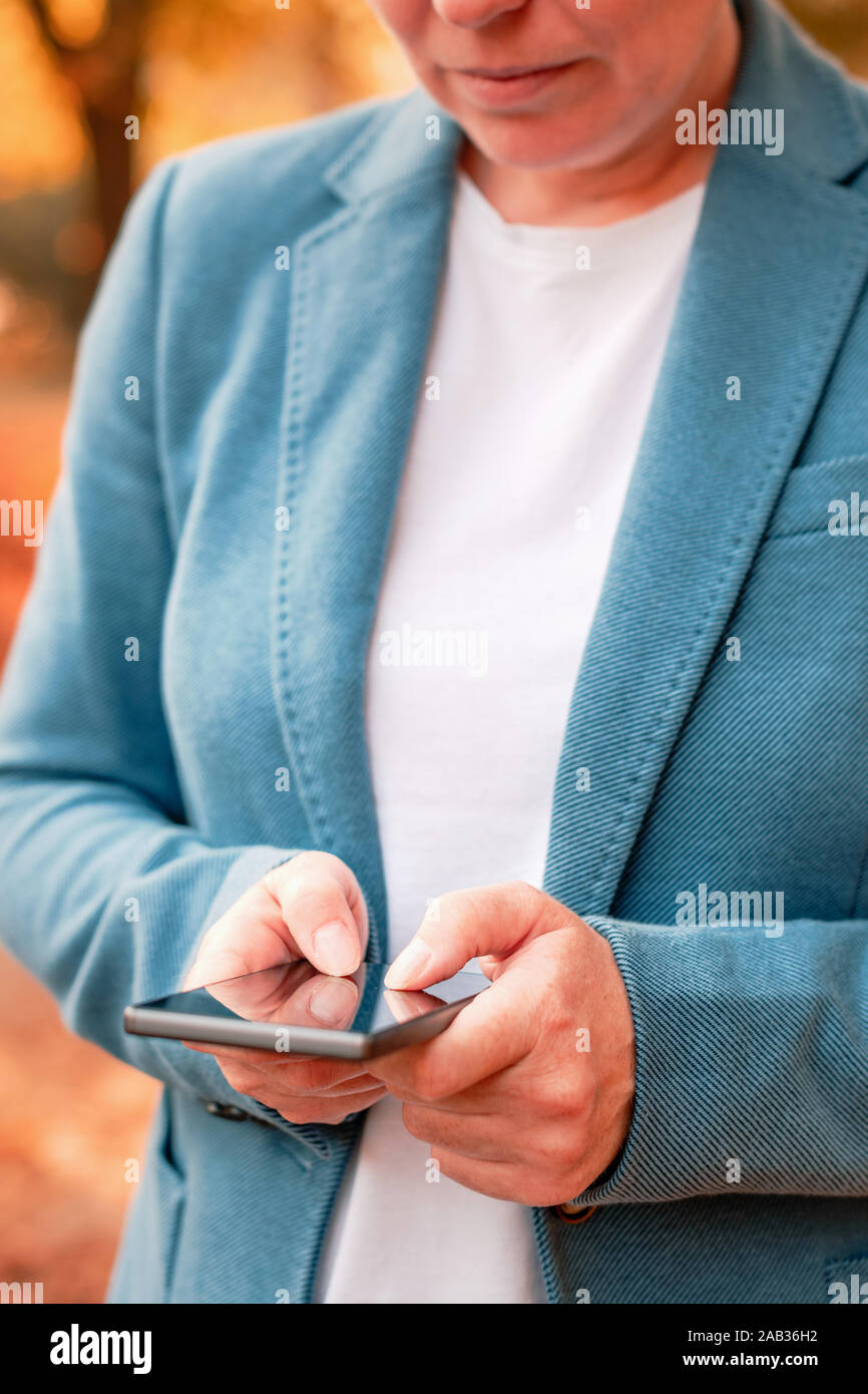 Imprenditrice la digitazione di un messaggio di testo sullo smartphone in autunno park, il fuoco selettivo sulle dita Foto Stock