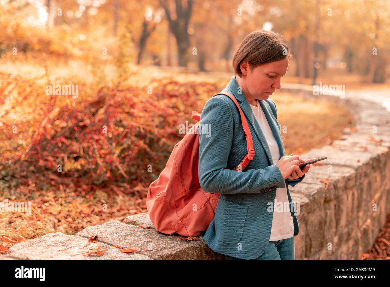 Imprenditrice tramite cellulare in autunno park, la digitazione di un messaggio di testo o e-mail di risposta, il fuoco selettivo Foto Stock